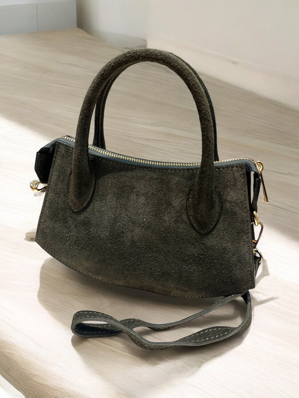 Borsa in pelle scamosciata grigia con maniglie e tracolla regolabile, dettagli metallici dorati, elegante e versatile.
